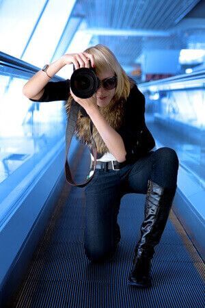 a woman is kneeling down on an escalator taking a picture with a camera .