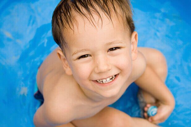un petit garçon est assis dans une piscine et sourit .
