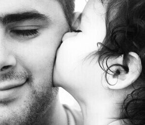 a woman is kissing a man on the cheek in a black and white photo .