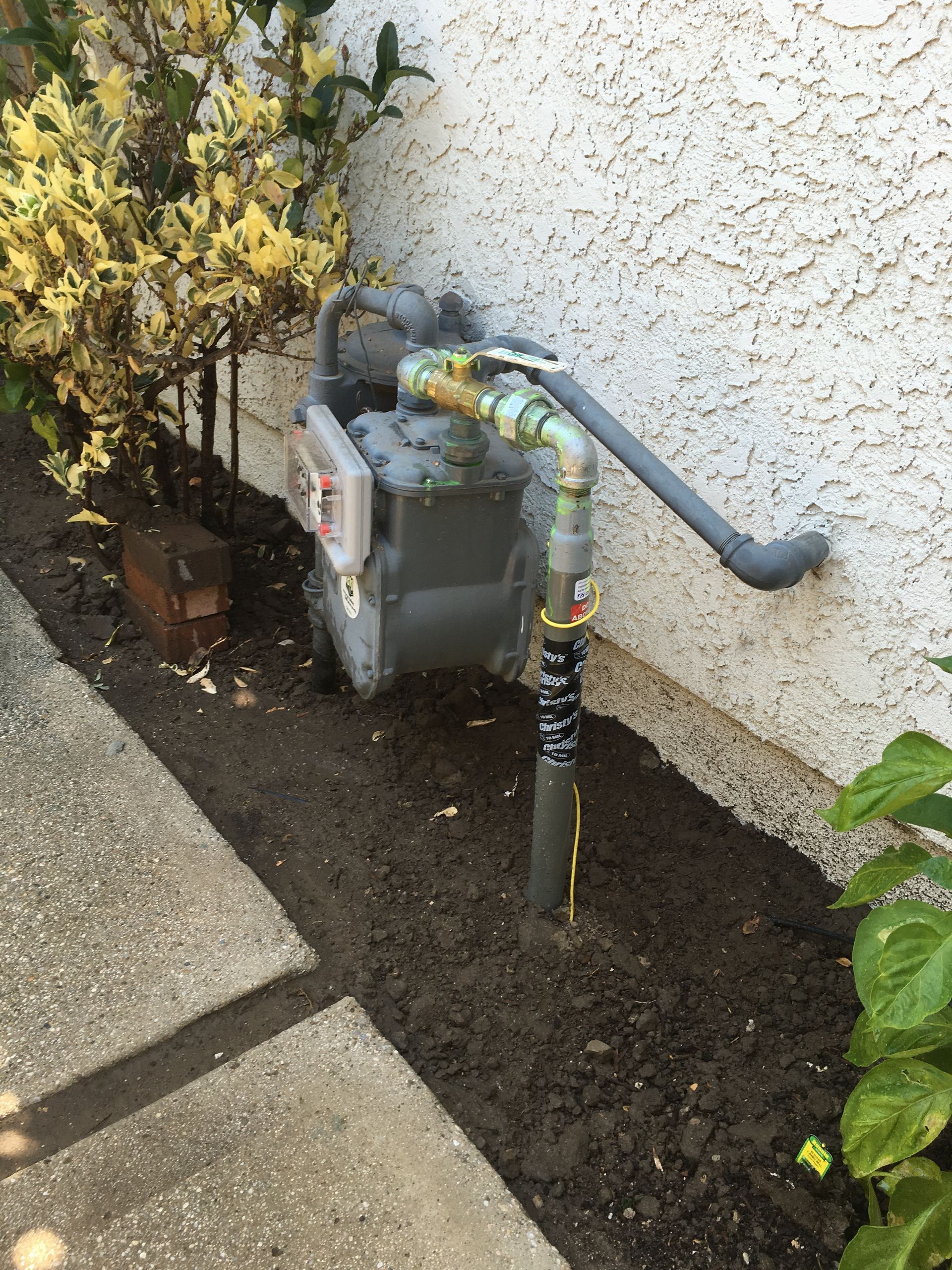 A gas meter is sitting on the side of a building next to a sidewalk.