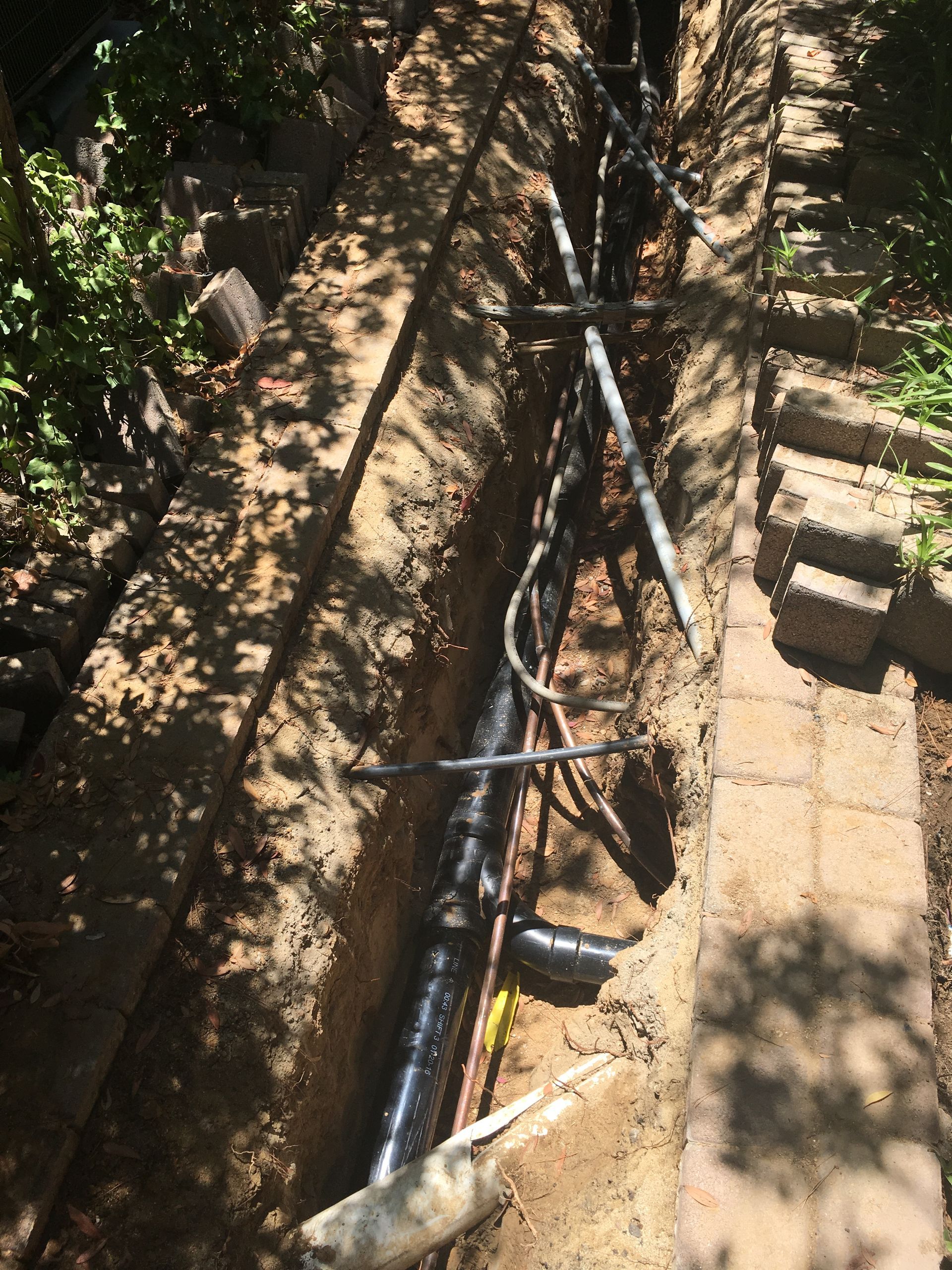 A black pipe is being installed in a trench.