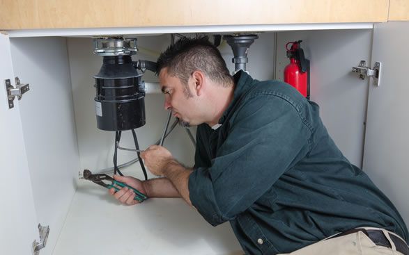 a man is fixing a garbage disposal under a sink in a kitchen .