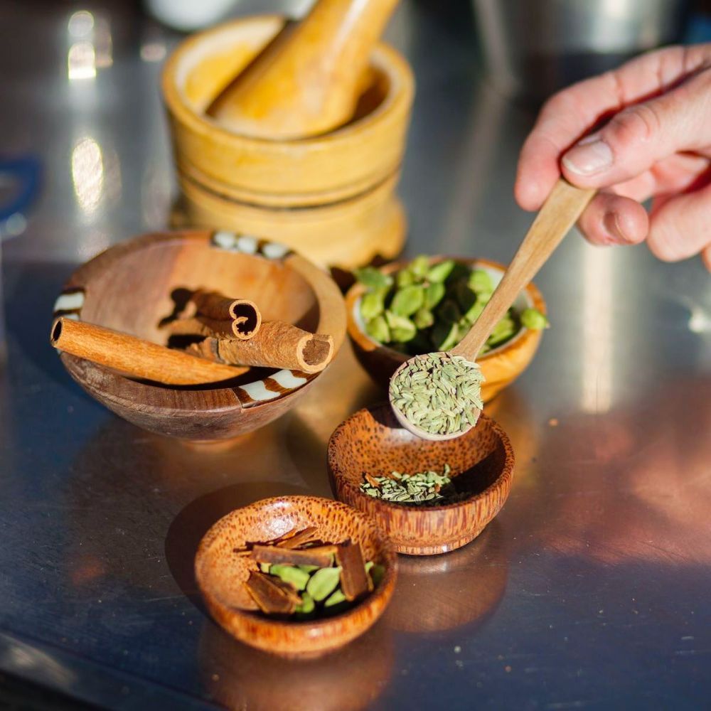 A person is holding a wooden spoon over a bowl of spices.