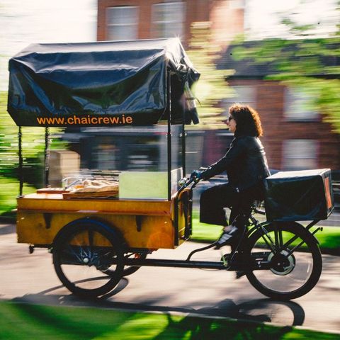 A woman is riding a bicycle with a canopy that says www.chaicrew.ie