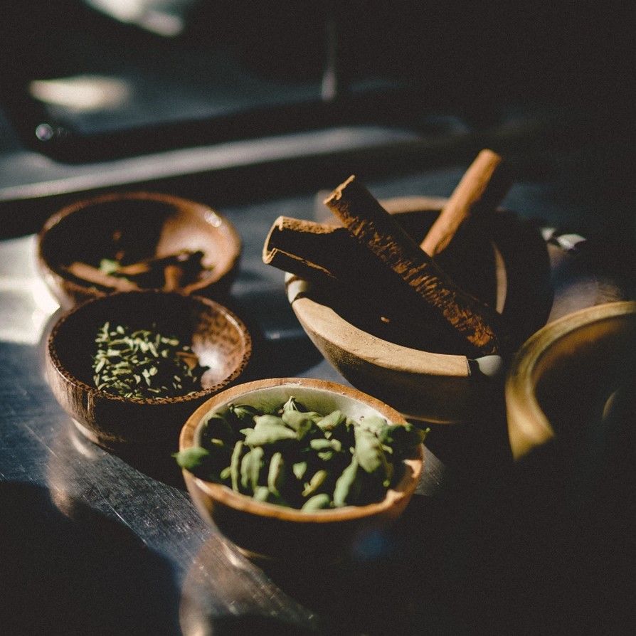 A wooden mortar and pestle sits on a table surrounded by bowls of spices