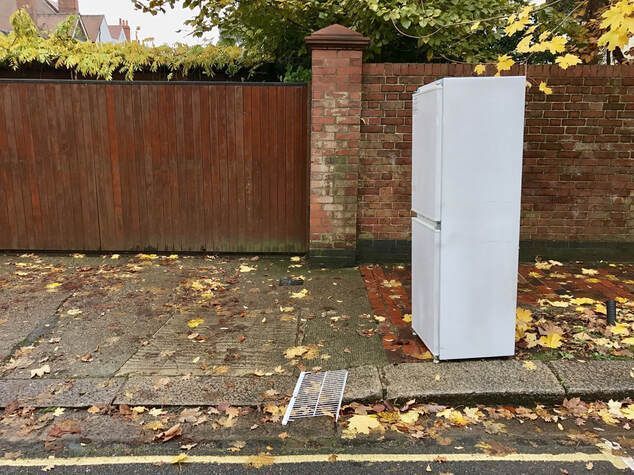 White refrigerator left on a brick sidewalk for appliance removal.