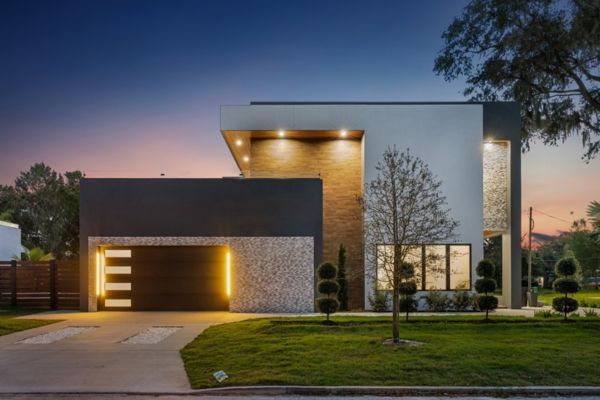 A modern house with a large garage door is lit up at night.