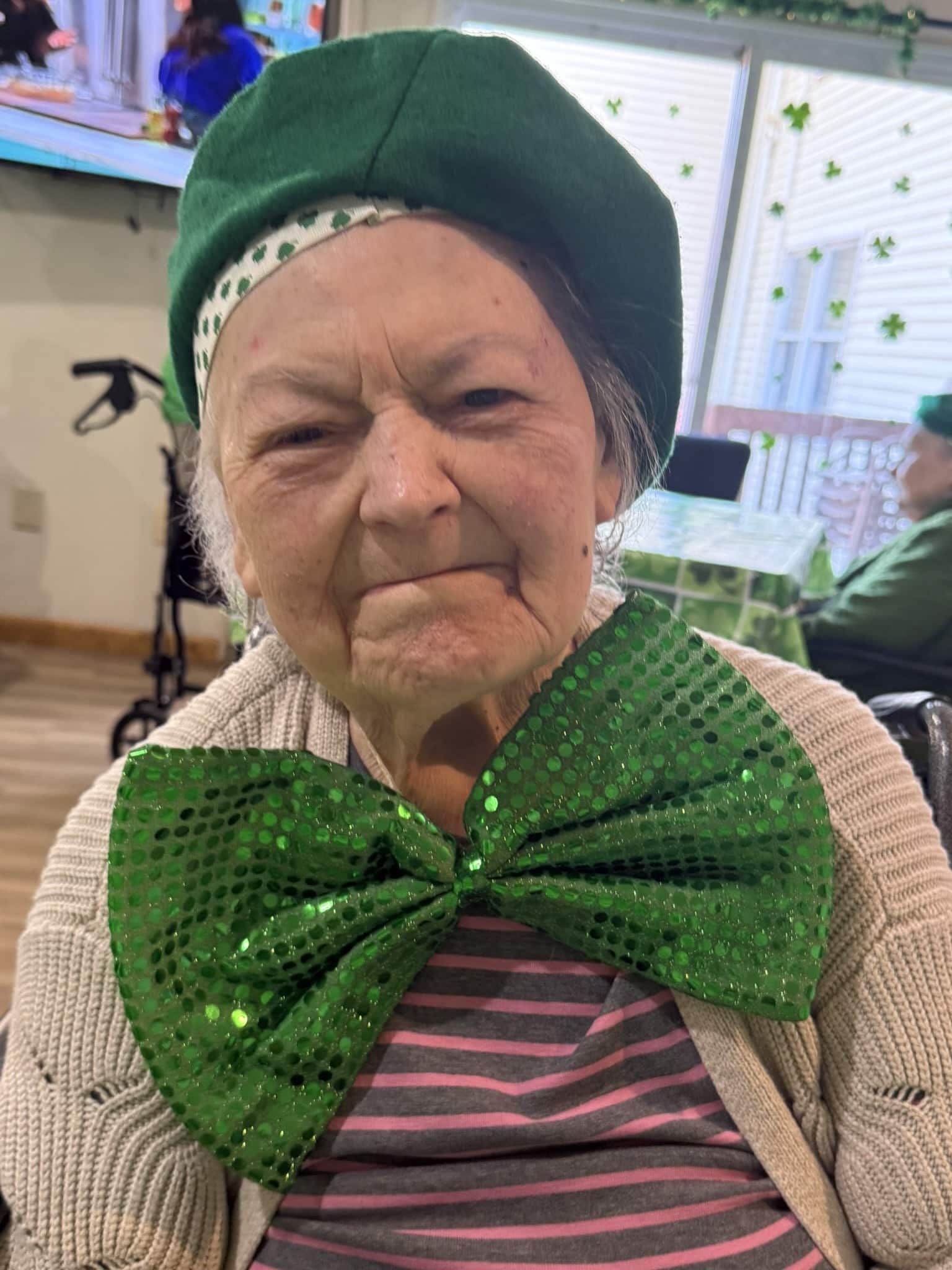 A person wearing a green beret and a large, sequined green bowtie over a striped shirt.