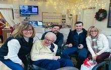 A group of five people pose for a photo in an indoor setting with holiday lights, smiling at the camera.