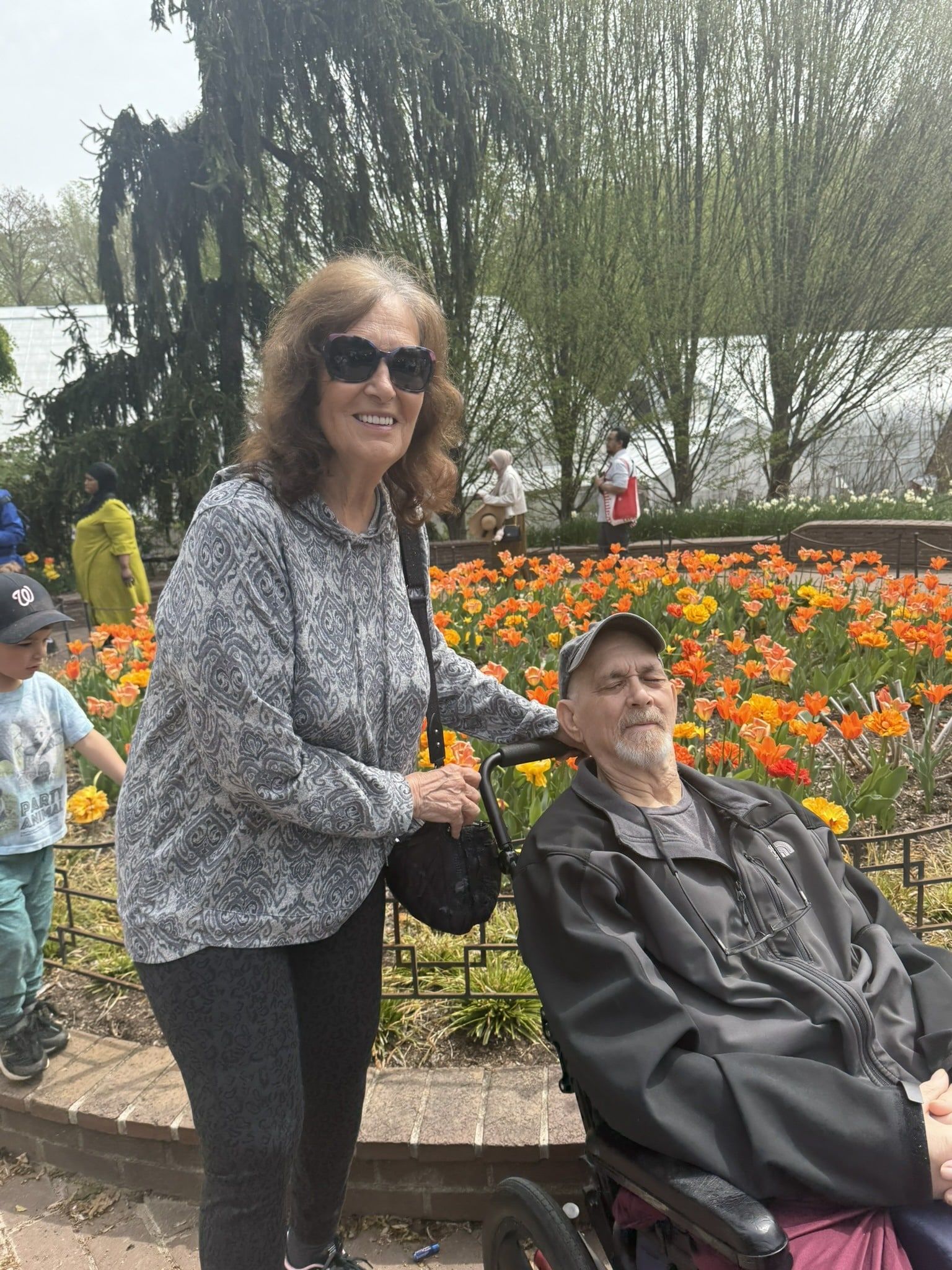 A person standing next to someone in a wheelchair at a park filled with blooming orange tulips.