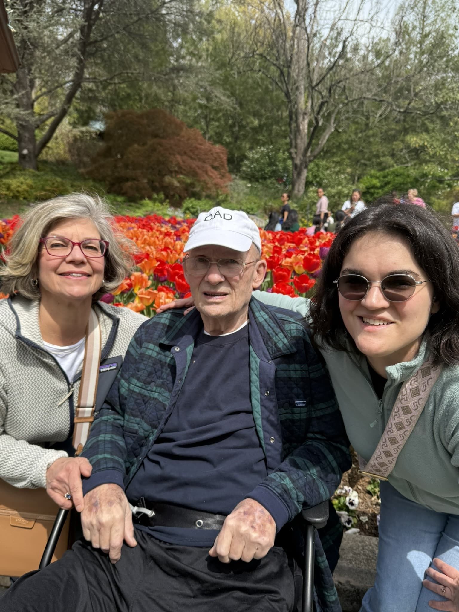 Three people pose for a photo in front of a vibrant field of orange tulips in a park.