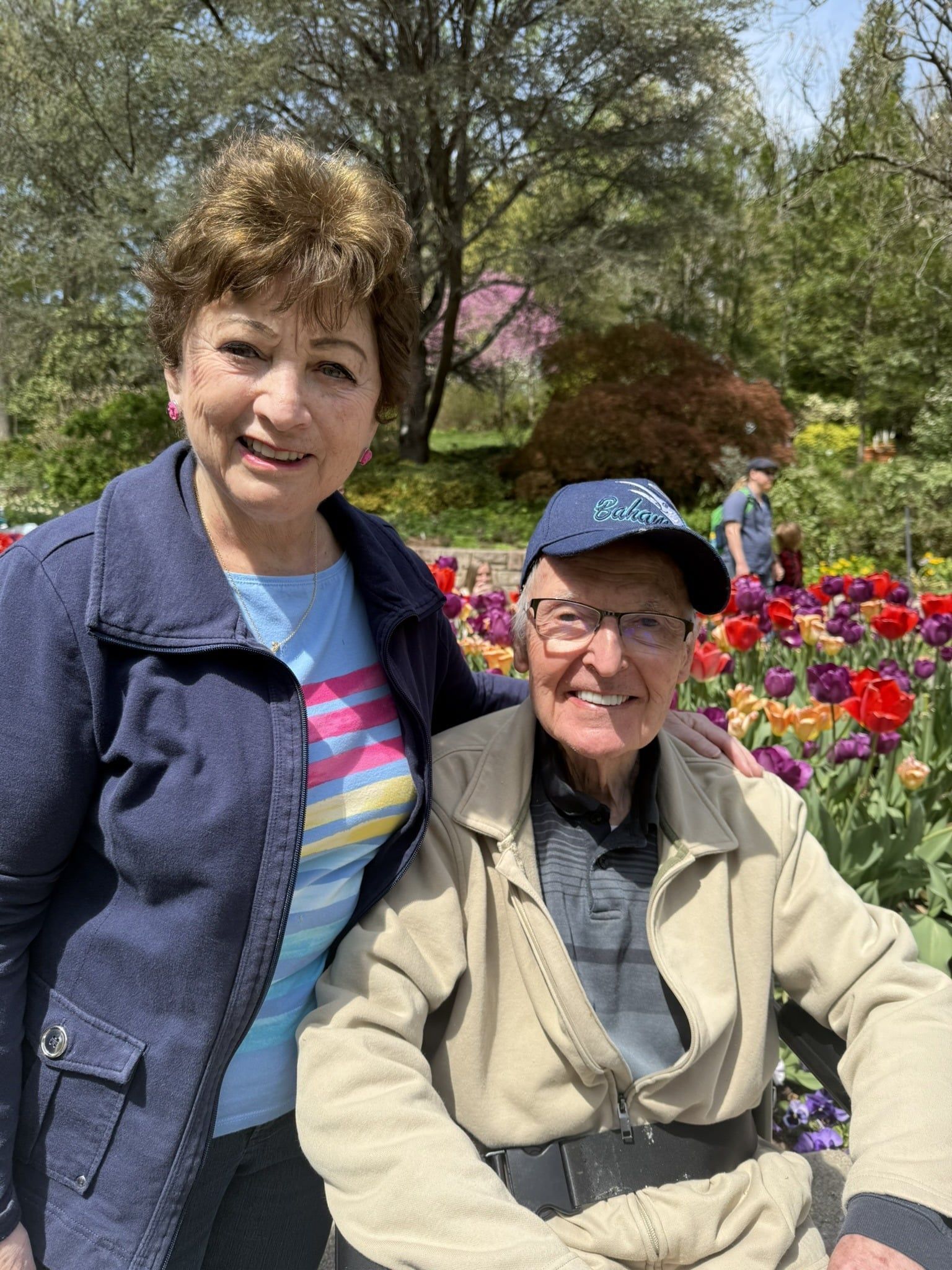 A smiling couple poses for a photo in a vibrant garden full of blooming tulips on a sunny day.