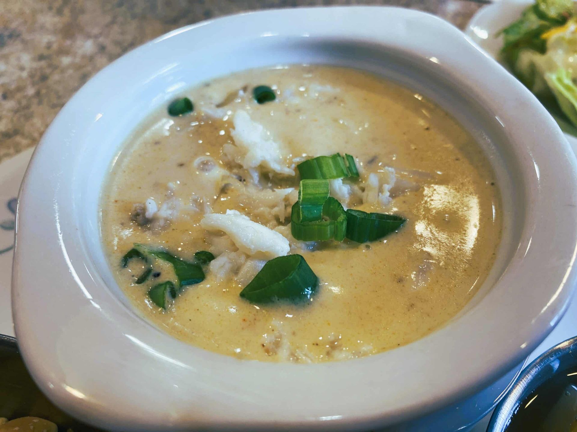 A bowl of creamy crab soup garnished with chopped green onions, served in a white ceramic dish.