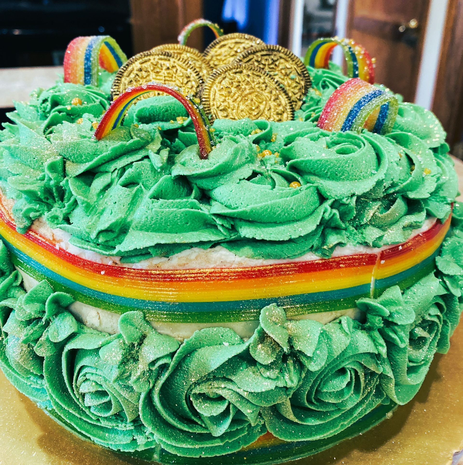 A St. Patrick's Day cake with green rosettes, rainbow candy strips, and chocolate gold coins on top.