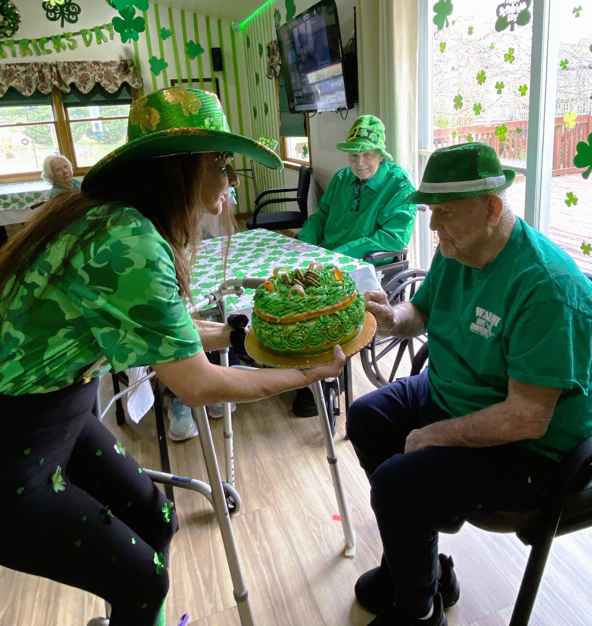 A person wearing a green hat offers a green cake to another person in a green shirt and hat during a holiday celebration.