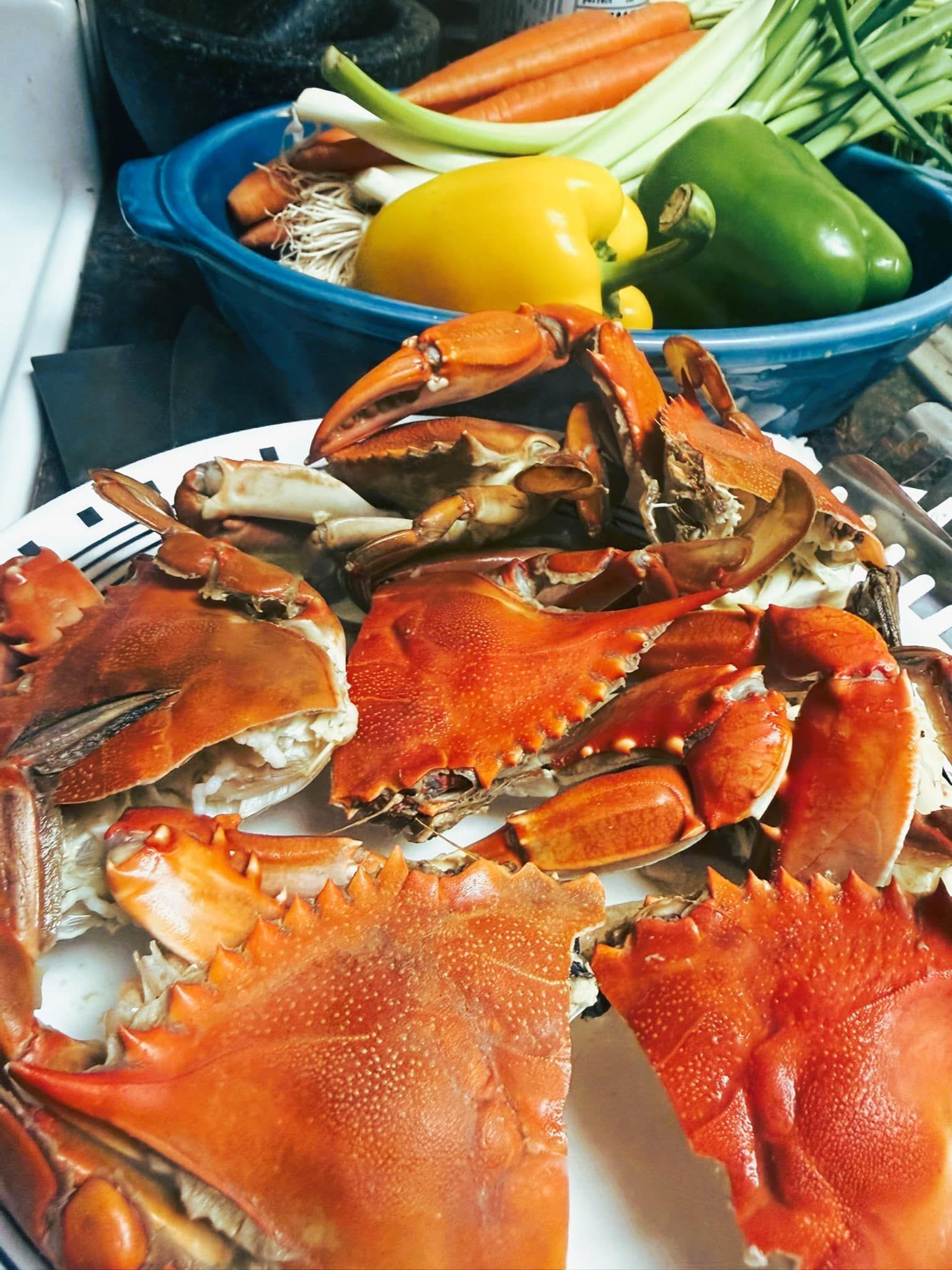 Cooked crabs on a plate, with a bowl containing carrots, celery, and yellow and green peppers in the background.