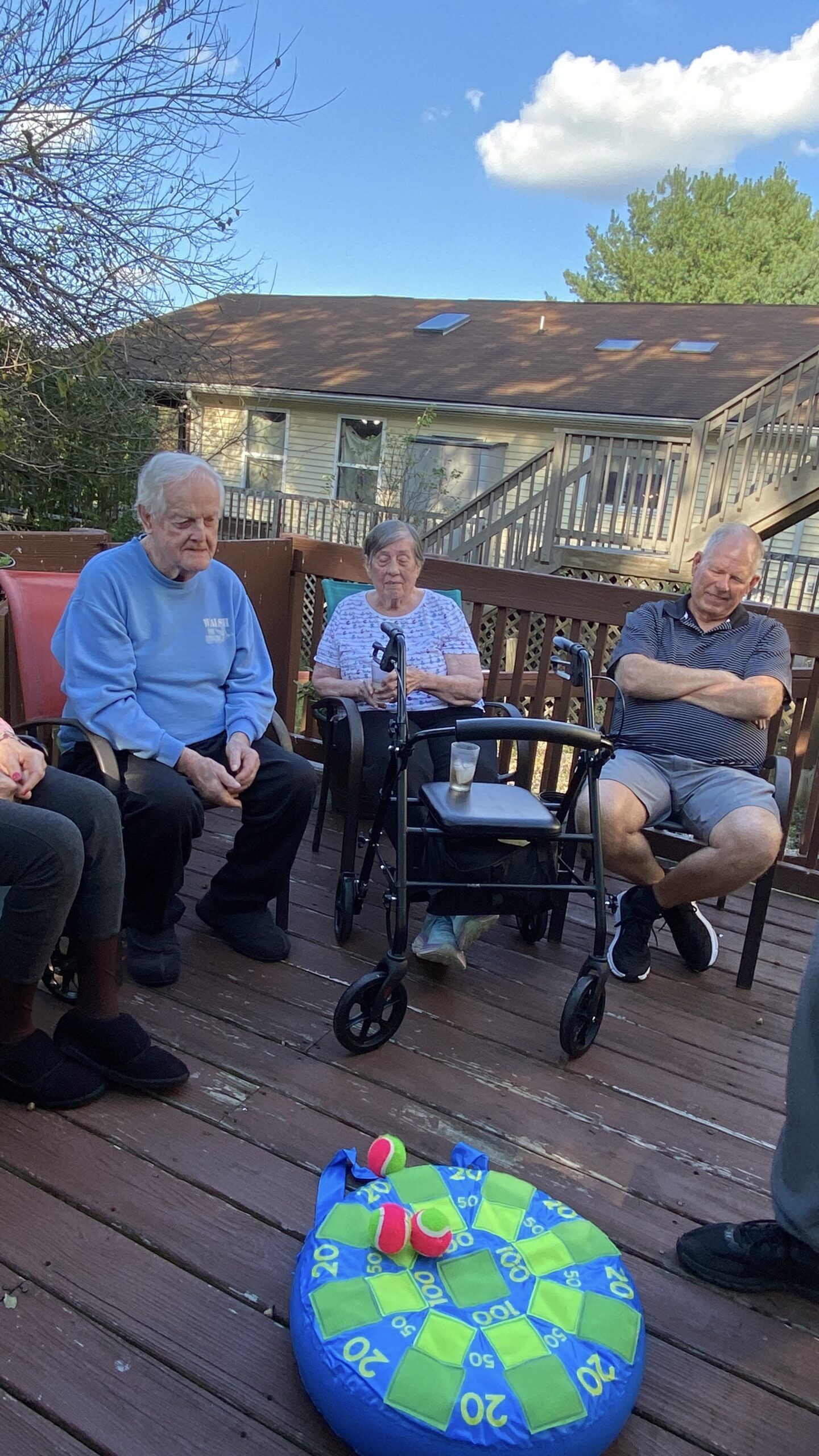 Three people sit on a wooden deck playing a velcro dart game with soft tennis-ball style darts.