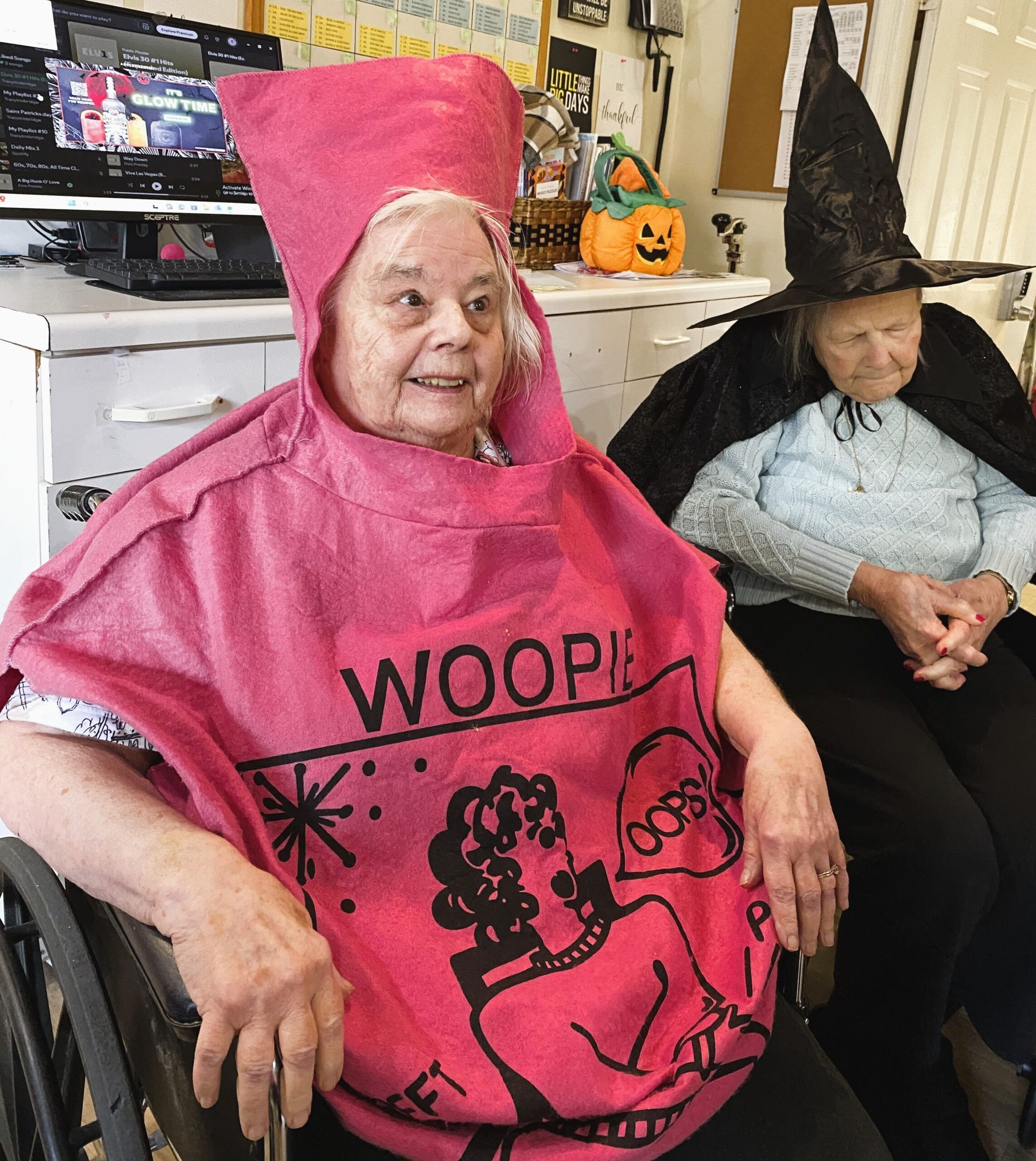 Two individuals in costumes sit indoors: one wears a pink 