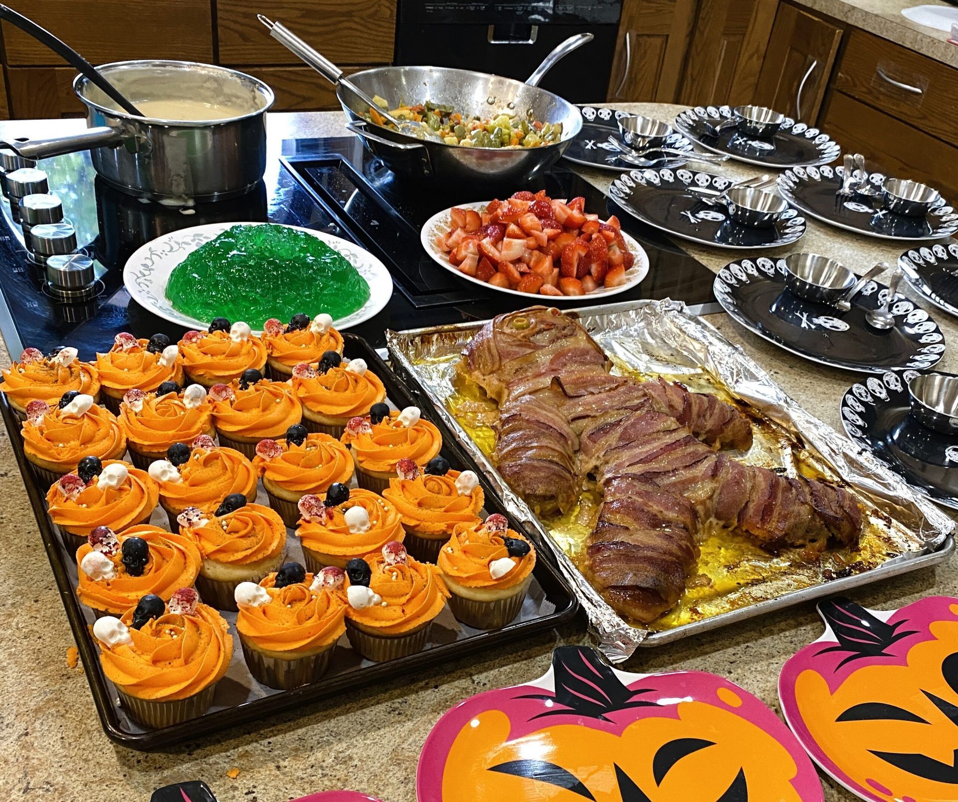 A kitchen counter with a spread of Halloween-themed food, including orange frosted cupcakes, gelatin, and meatloaf.