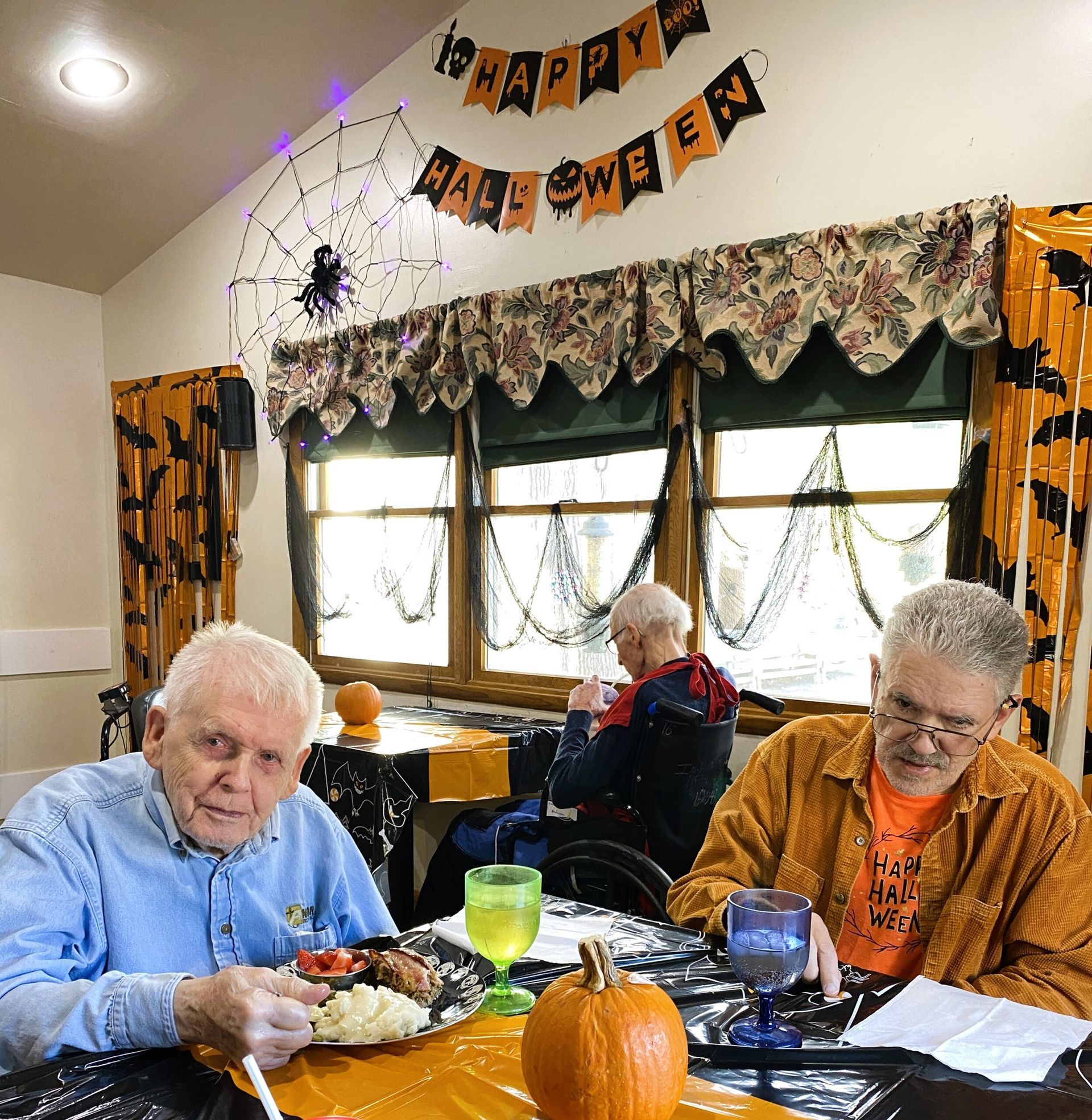 Two people seated at a table with Halloween decorations and a small pumpkin, inside a decorated room.