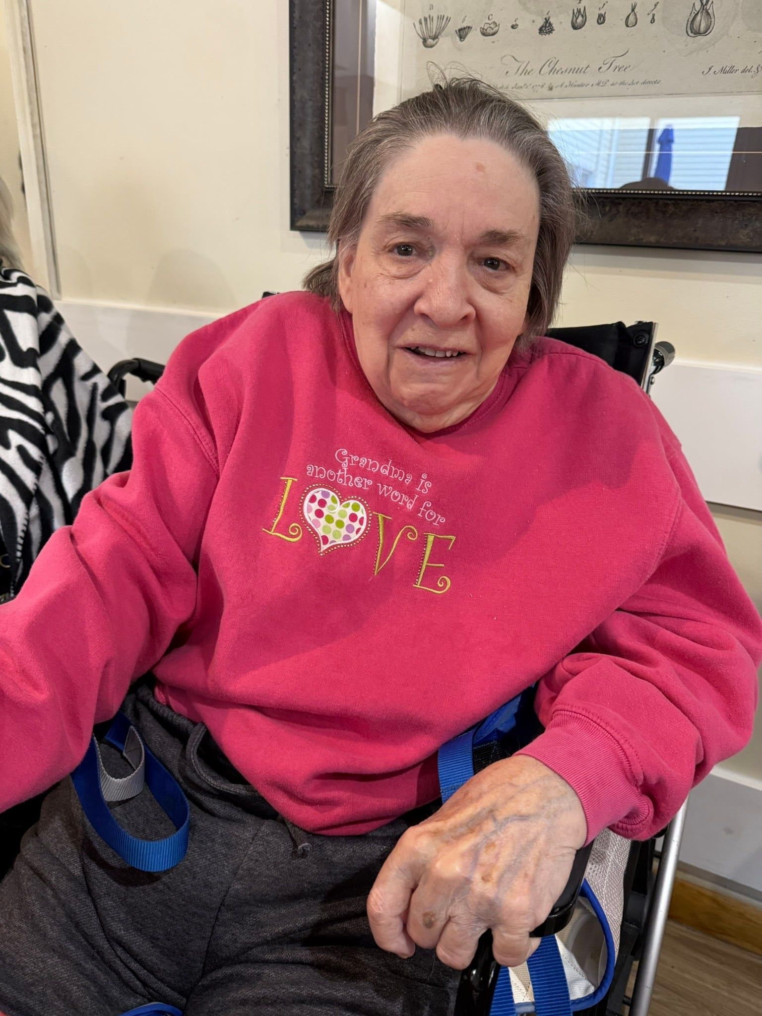 A person sits in a wheelchair wearing a bright pink sweatshirt with the word 