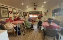 Residents seated at tables with red and white checkered tablecloths in a community room decorated with heart wall art.