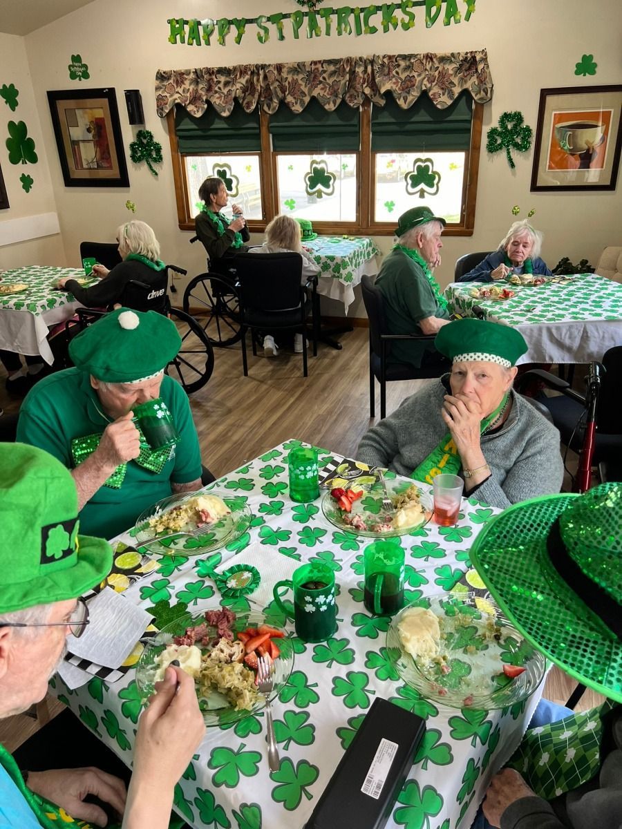 People in green hats and festive attire celebrate St. Patrick’s Day at decorated tables in a dining room.