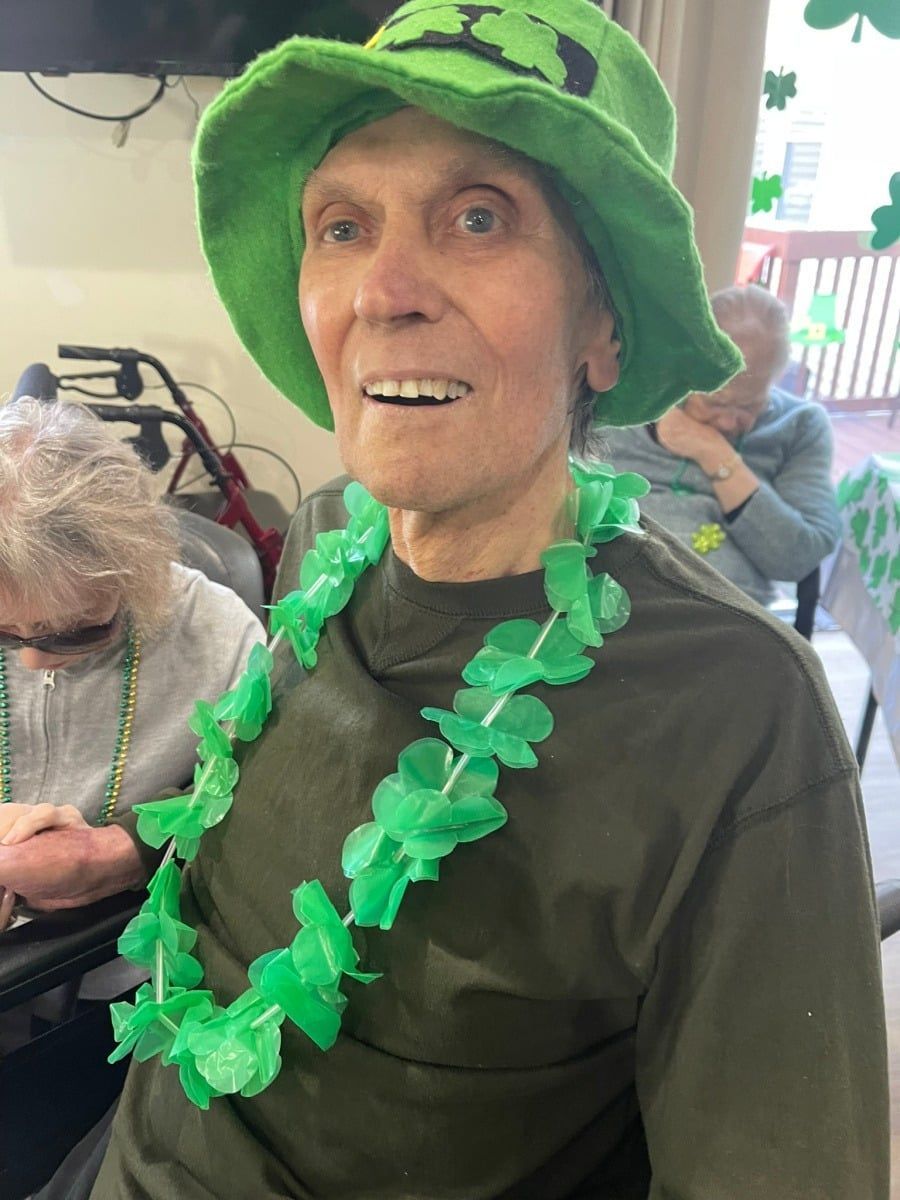 A person in a green hat and green floral lei sits at a table during a St. Patrick's Day celebration.