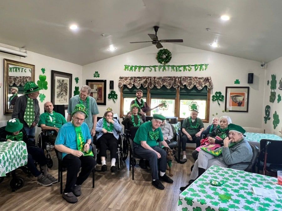 A group of people wearing green and shamrock accessories celebrating St. Patrick's Day in a decorated community room.