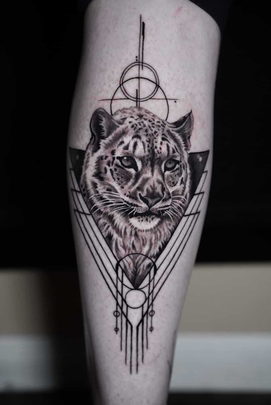 Black and white tattoo of a snow leopard's face within geometric shapes on a leg.