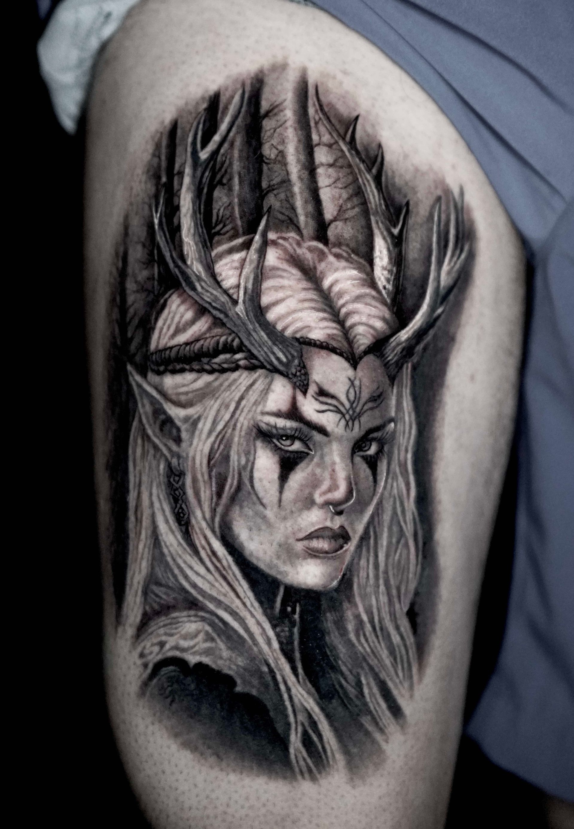 Tattoo of a fantasy elven woman with antler crown, in black and gray shading, on a thigh.