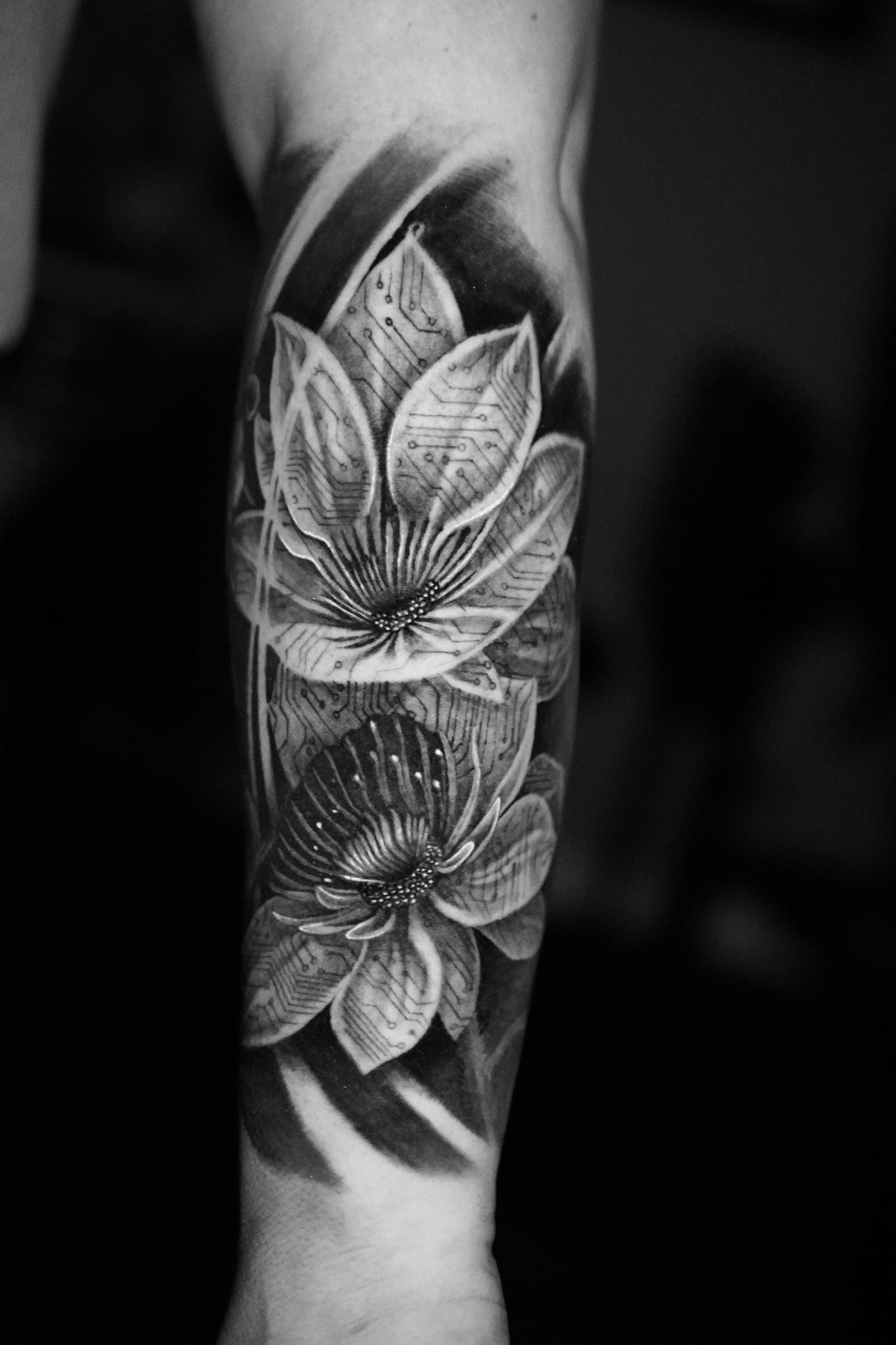 Black and white tattoo of two detailed lotus flowers on an arm.