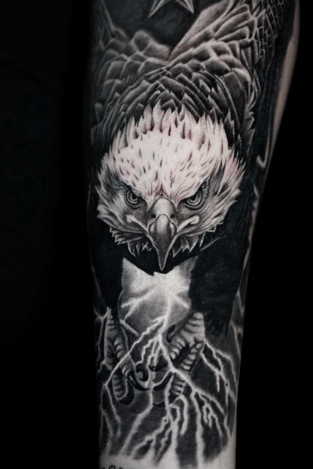 Black and white eagle tattoo. Eagle head with fierce expression, talons with lightning, on arm.