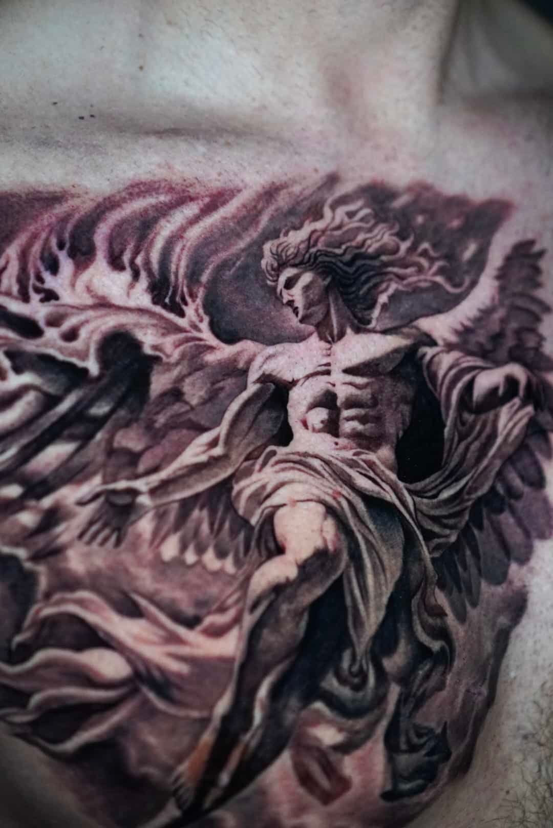 Tattoo of an angel with outstretched wings, surrounded by dark smoke or clouds; on a person's chest.