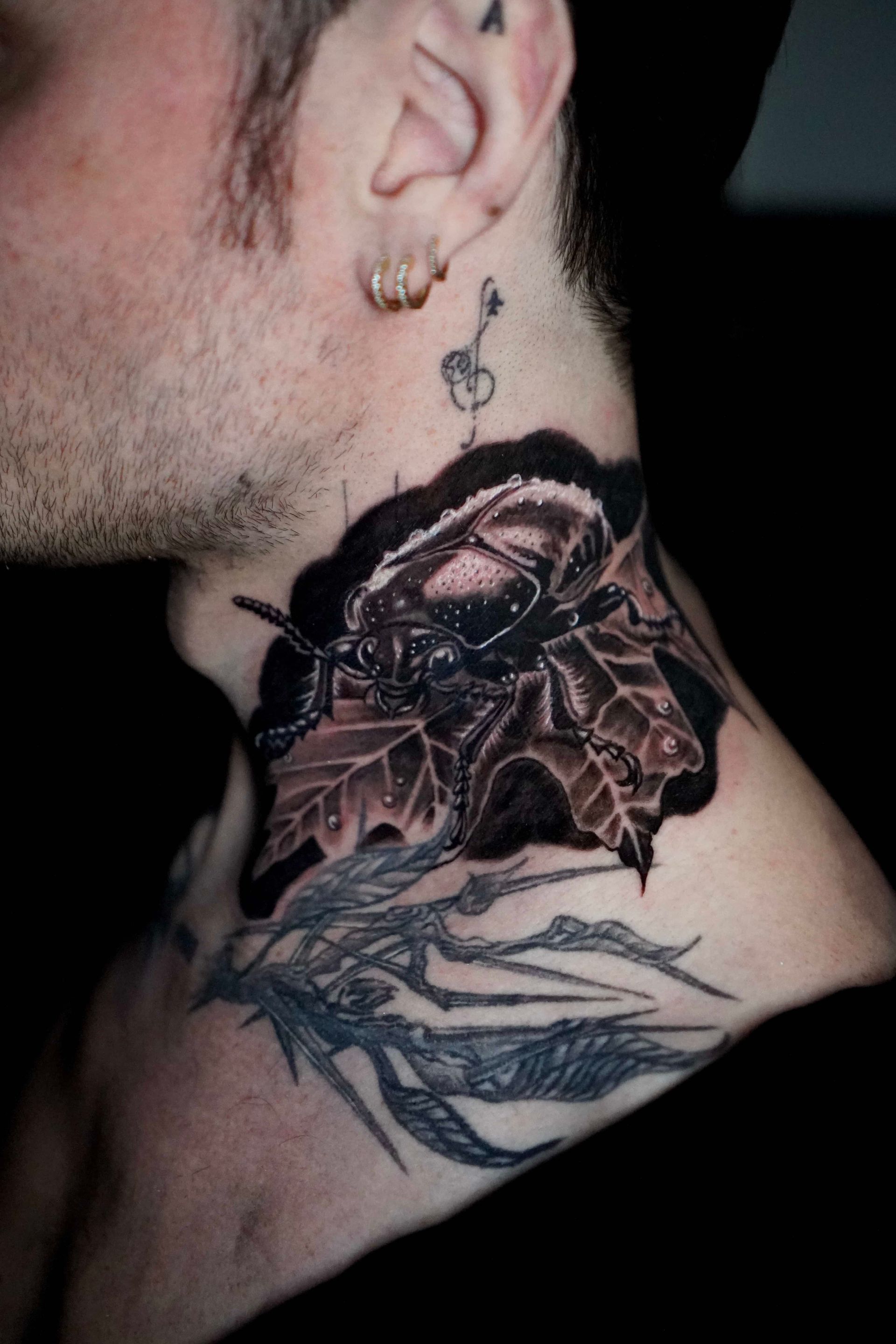 Tattoo of a beetle on a leaf on a person's neck and chest, with a key tattoo on the neck.