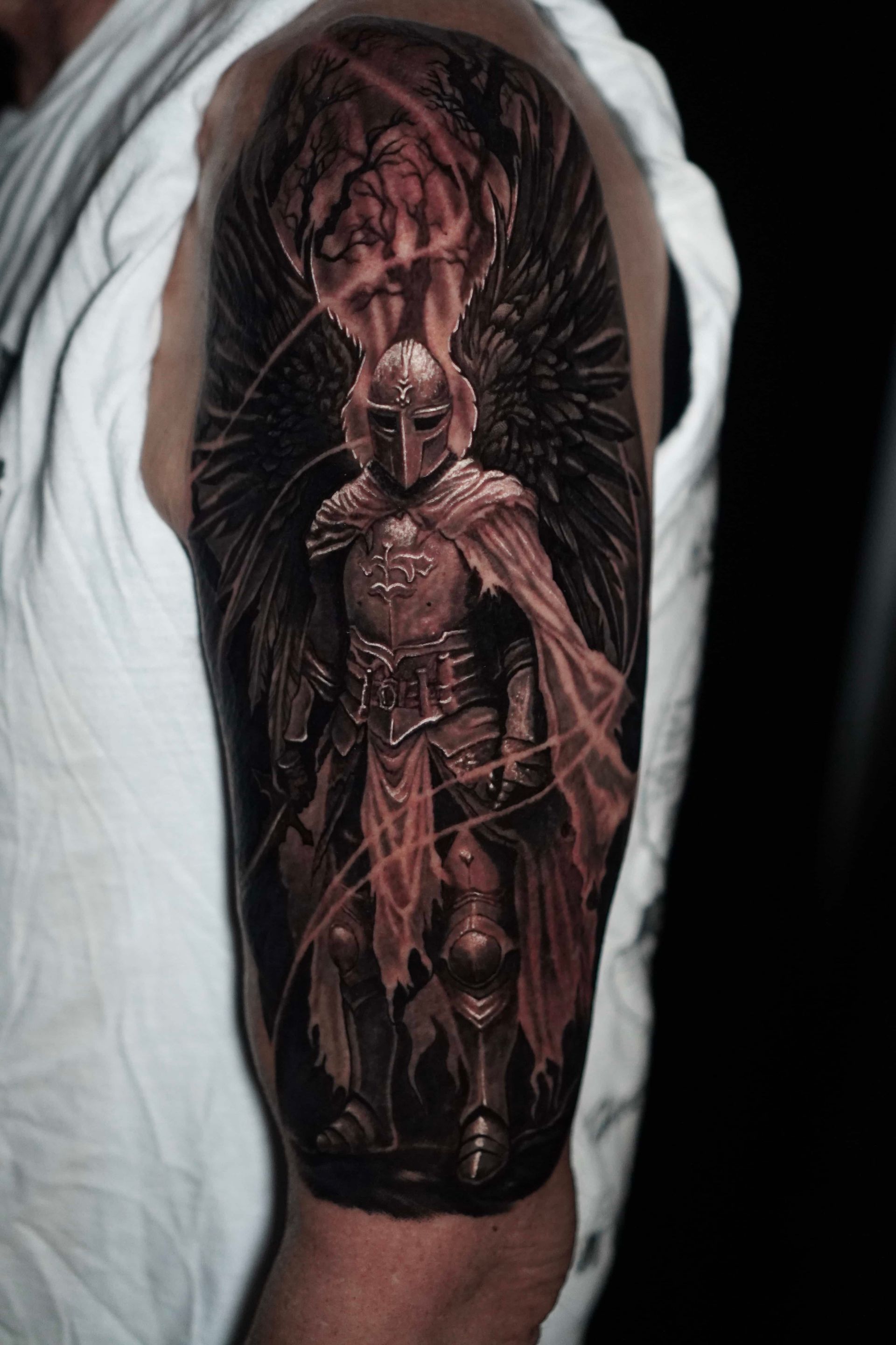 Tattoo of an armored figure with large wings, a helmet, and a flowing cape, detailed and shaded.