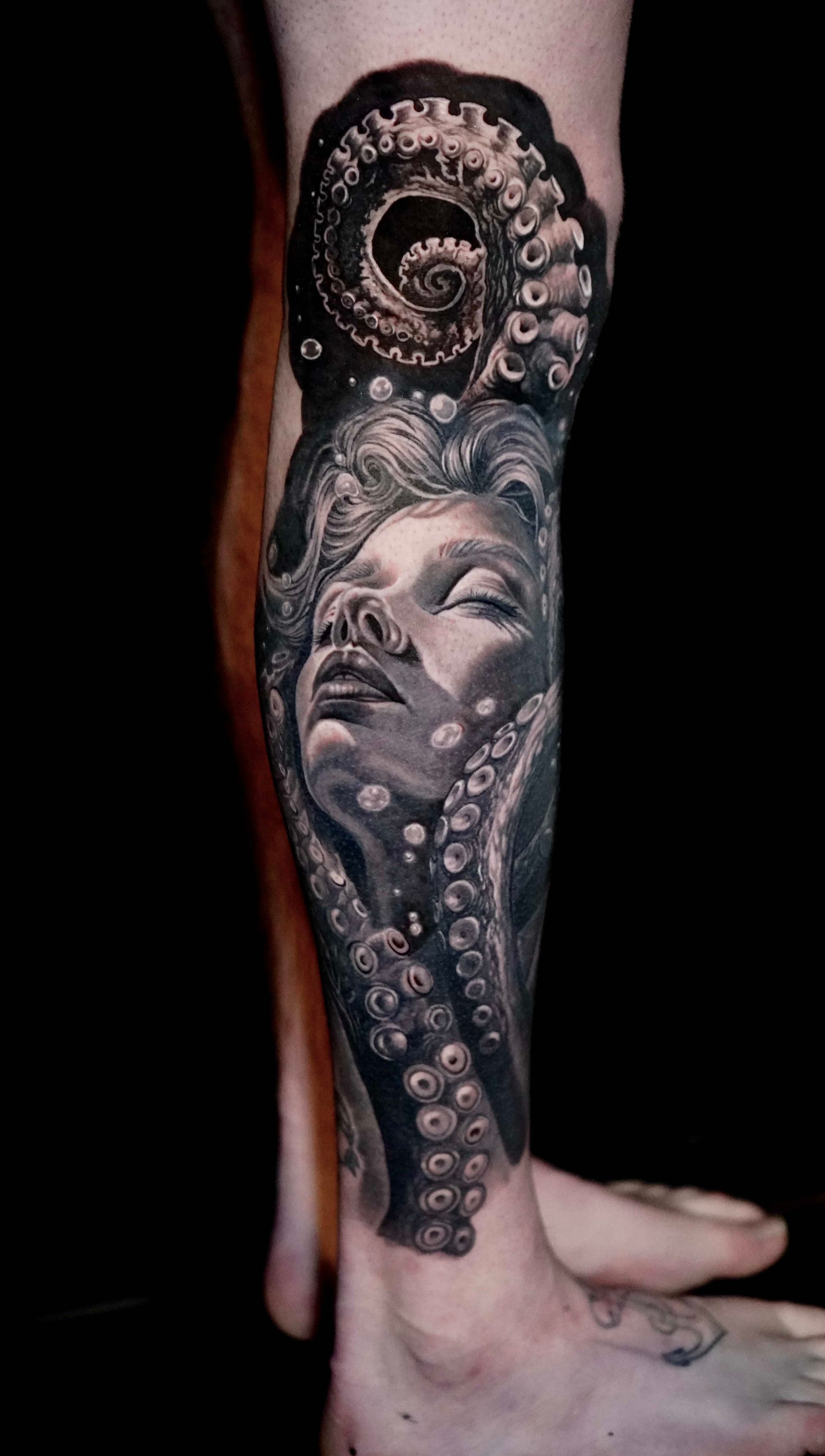 Black and white tattoo of a woman's face and octopus tentacles on a leg.