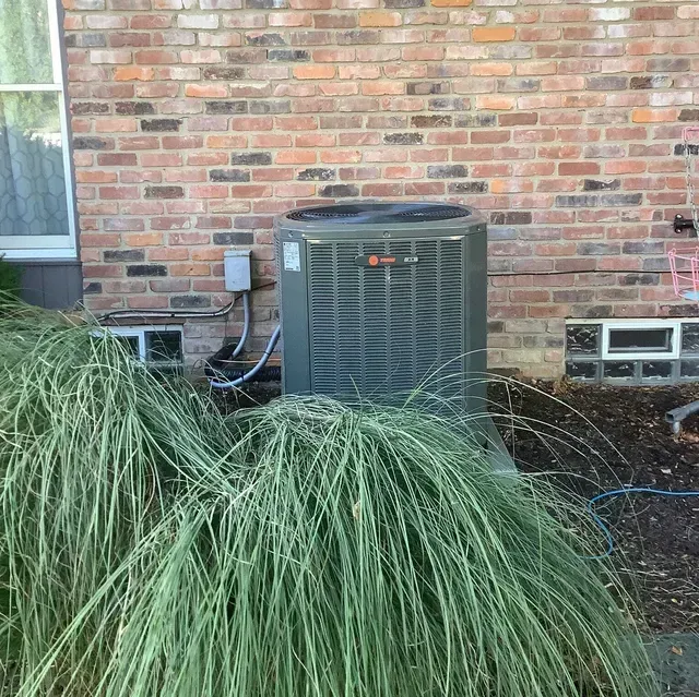 A large air conditioner is sitting in front of a brick building.