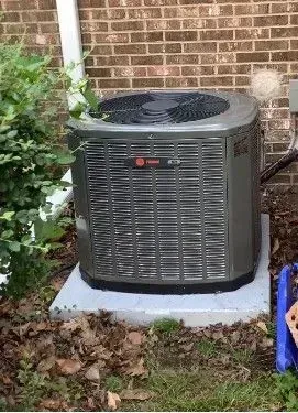 A large air conditioner is sitting on top of a concrete platform in front of a brick building.