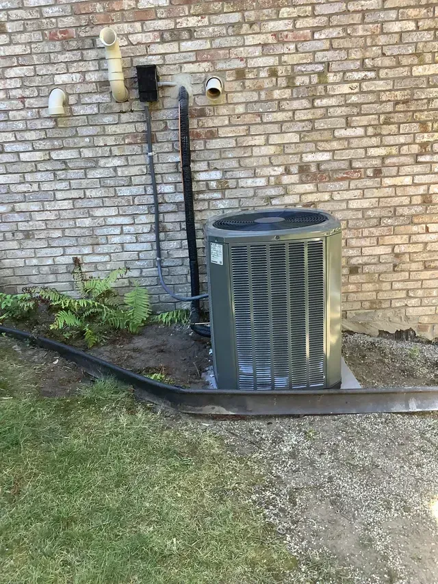 An air conditioner is sitting on the side of a brick building.