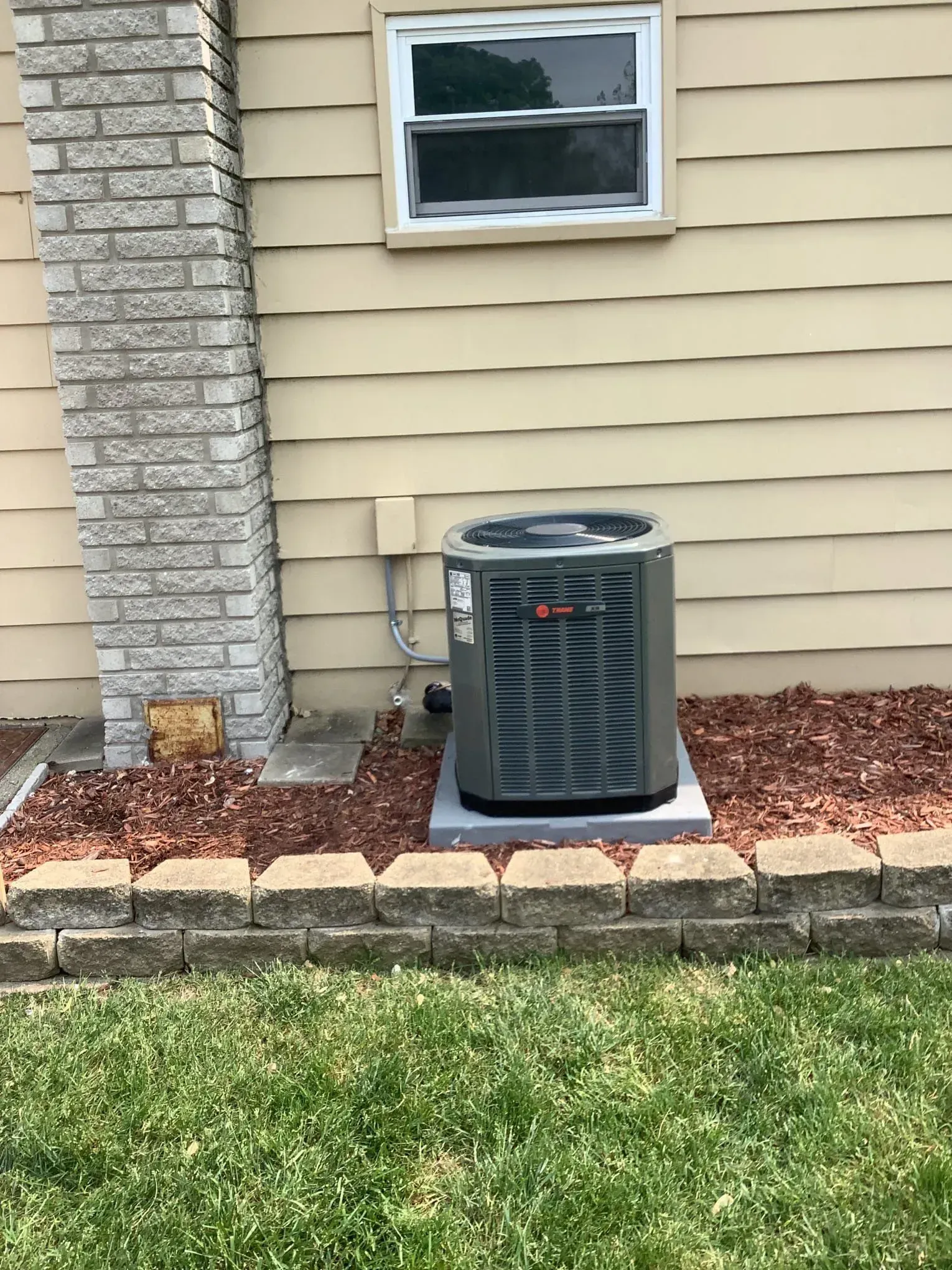 An air conditioner is sitting on the side of a house next to a brick chimney.