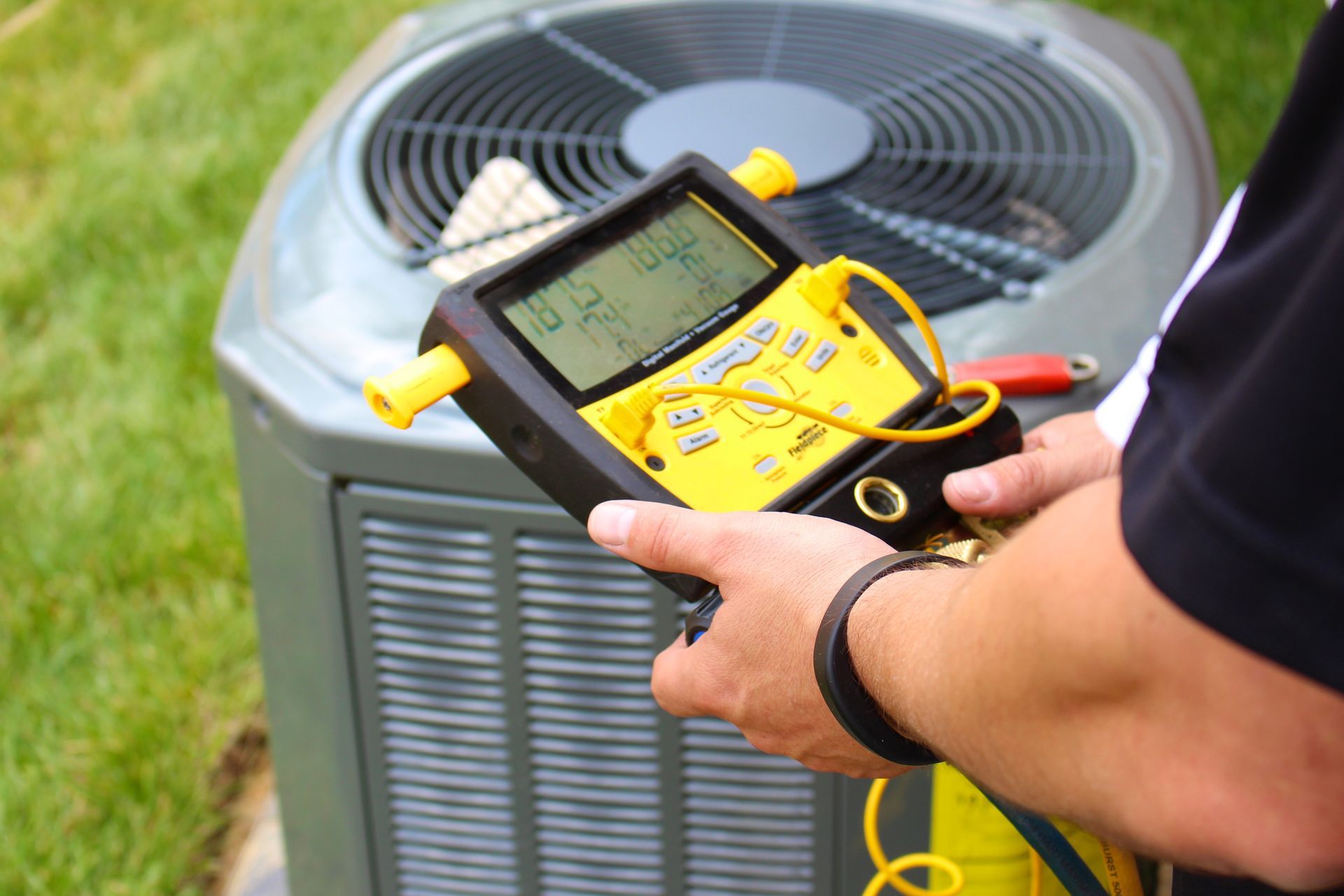 Technician checking refrigerant levels on an outdoor air conditioning unit using a digital gauge.