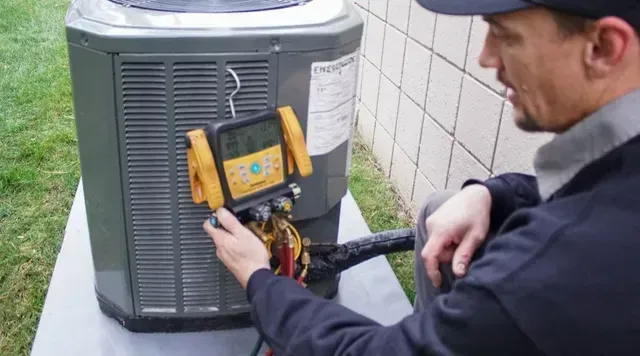 Air conditioning repair technician in safety gear fixing AC unit | Rochester, MI | McQuade HVAC Air conditioning repair technician in safety gear fixing AC unit | Rochester, MI | McQuade HVAC