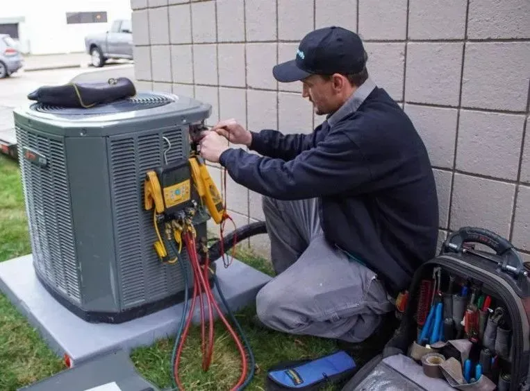 A man is working on an air conditioner outside of a building.