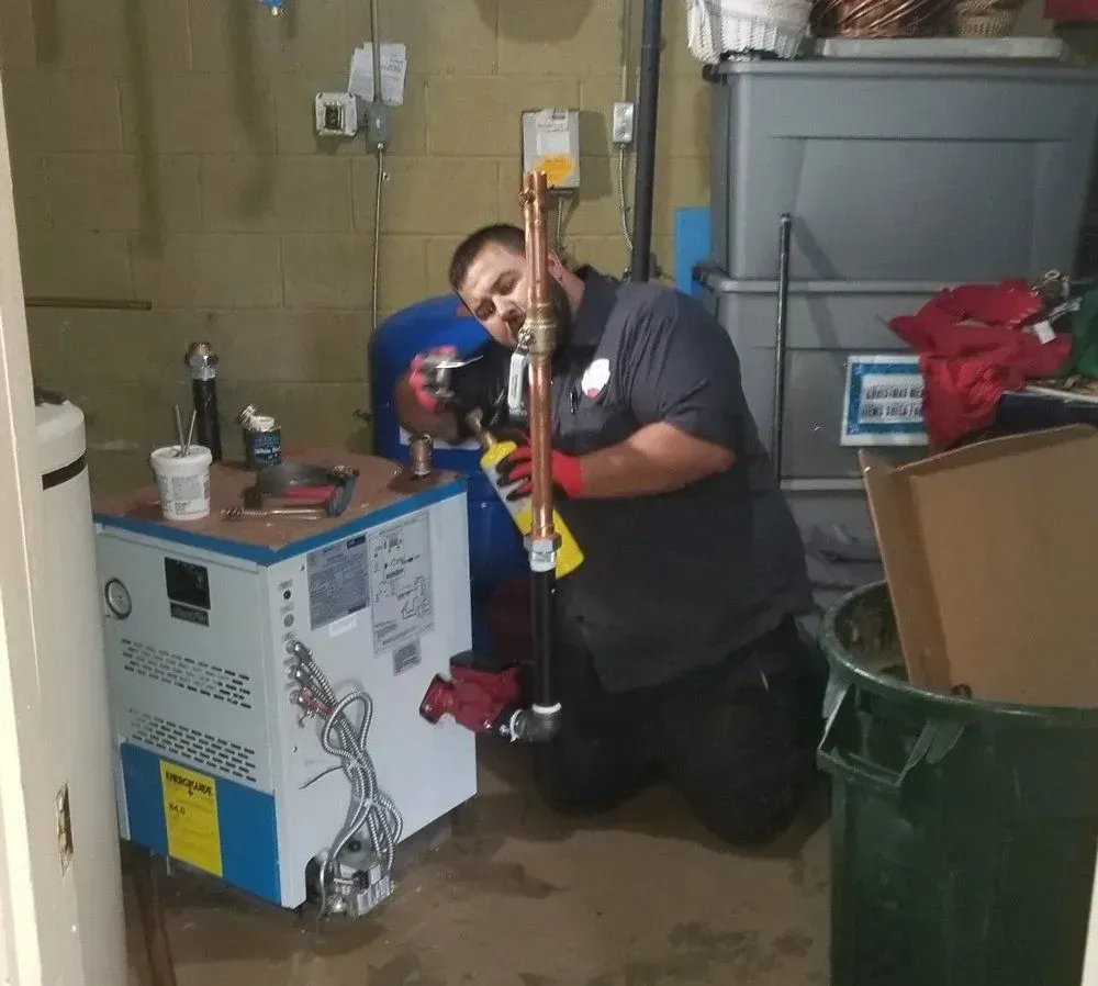 A man is kneeling down in front of a water heater