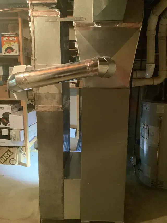 A stainless steel pipe is hanging from a wall in a basement.