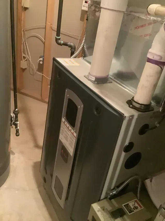 A boiler is sitting in a basement next to a water heater.
