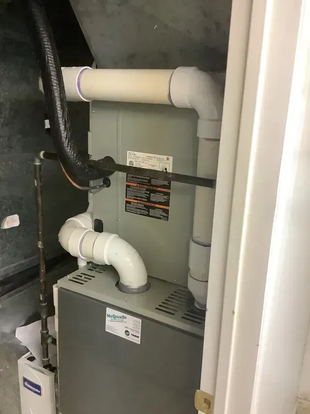 A furnace is sitting in the corner of a room next to a door.