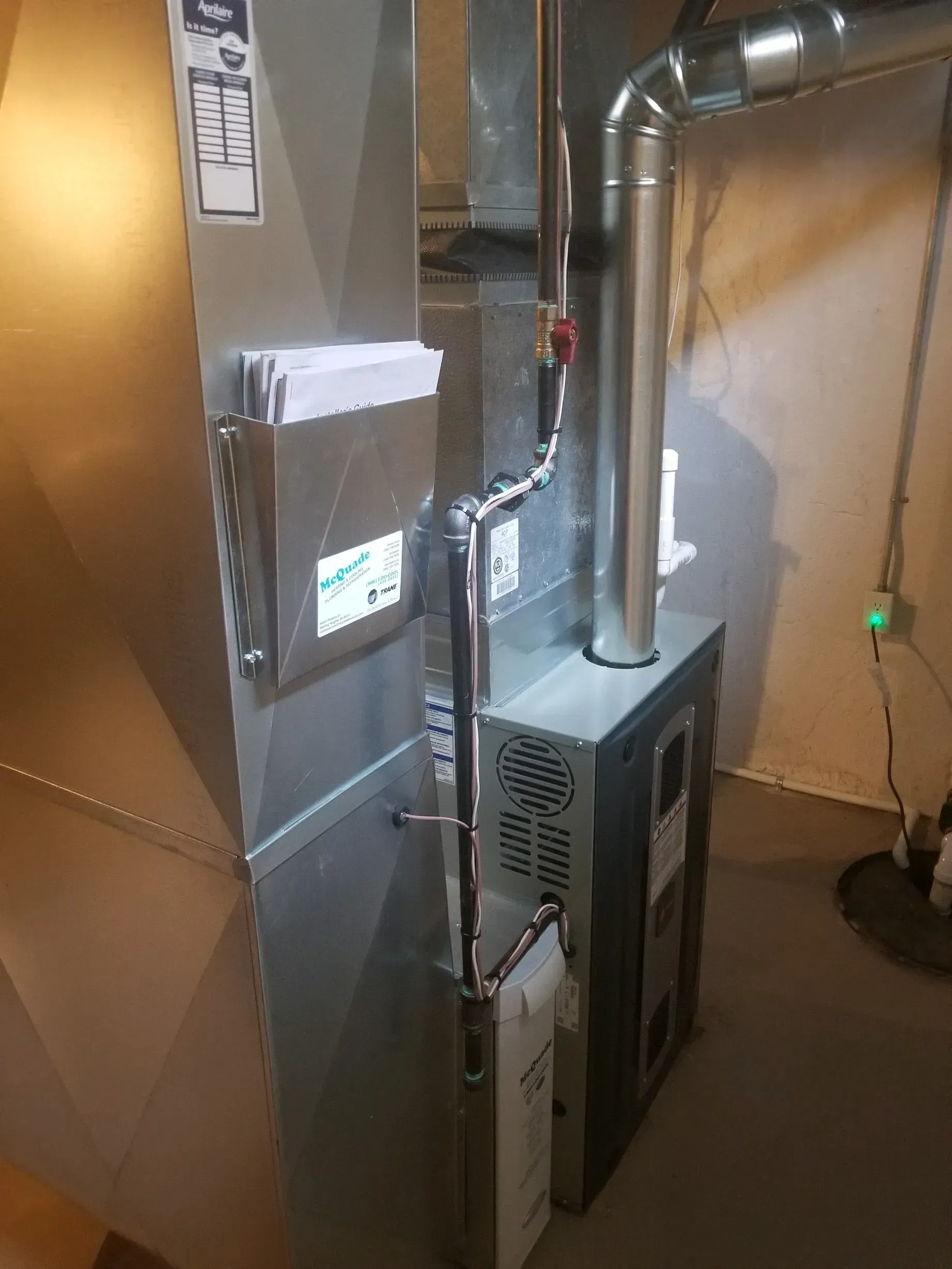 A stainless steel furnace is sitting in a basement next to a wall.