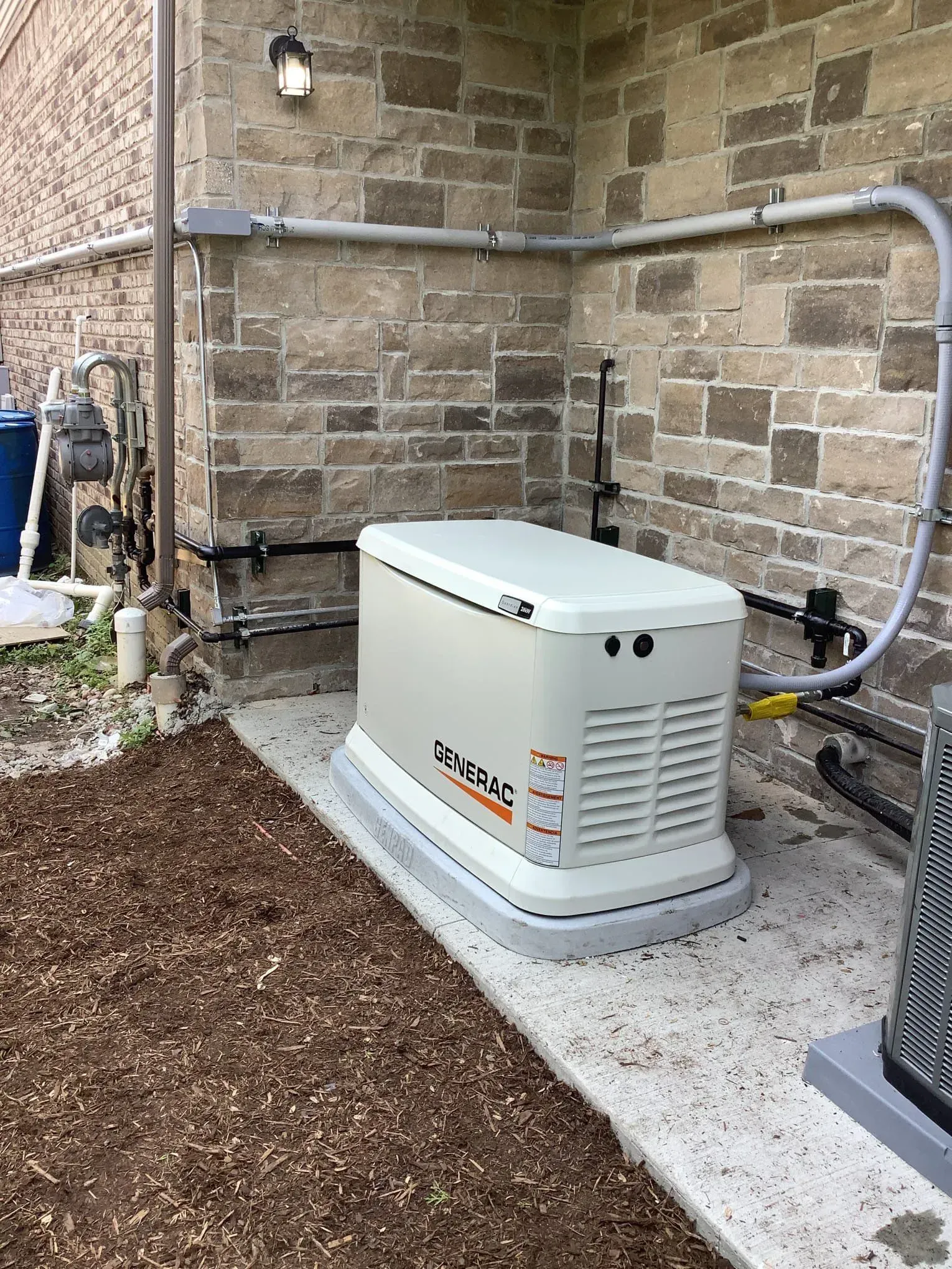 A generator is sitting on the side of a brick building.